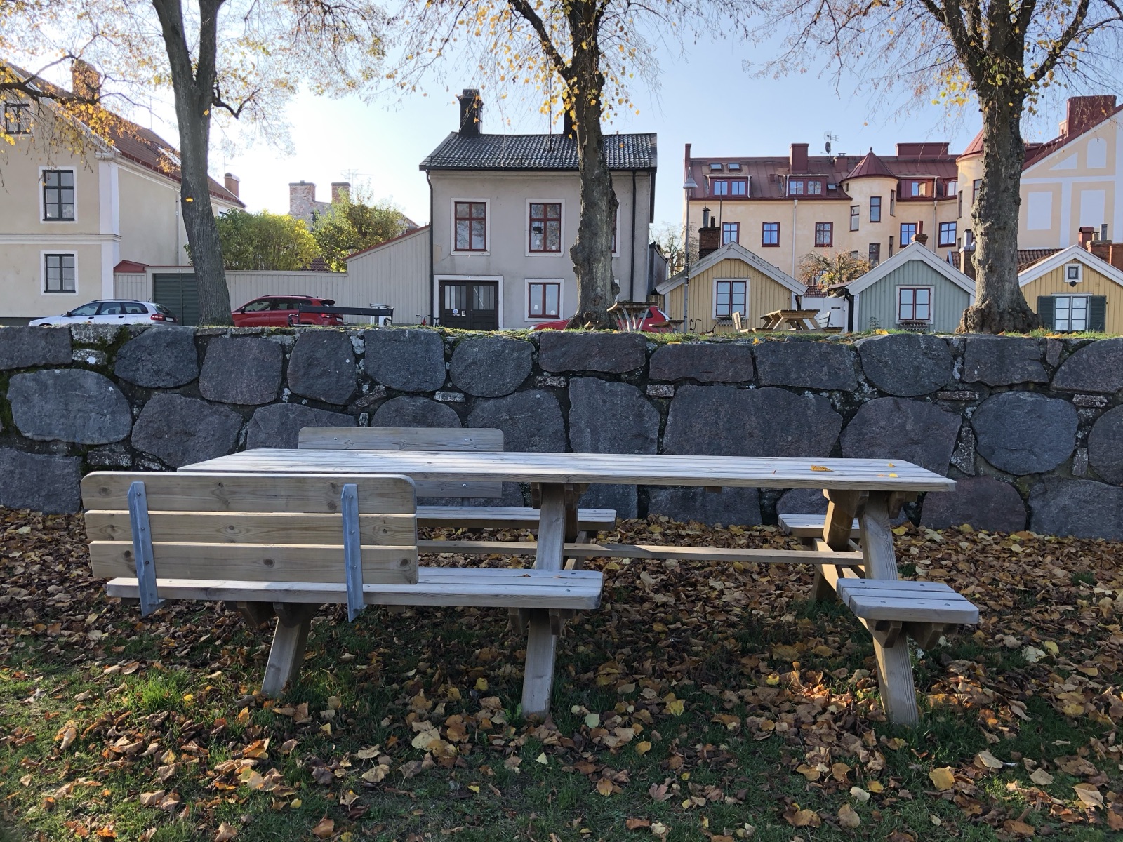 Long picnic table below Kalmar’s old city wall, with bench sections with and without backrests and two open cutouts facing each other near the middle of the seating line